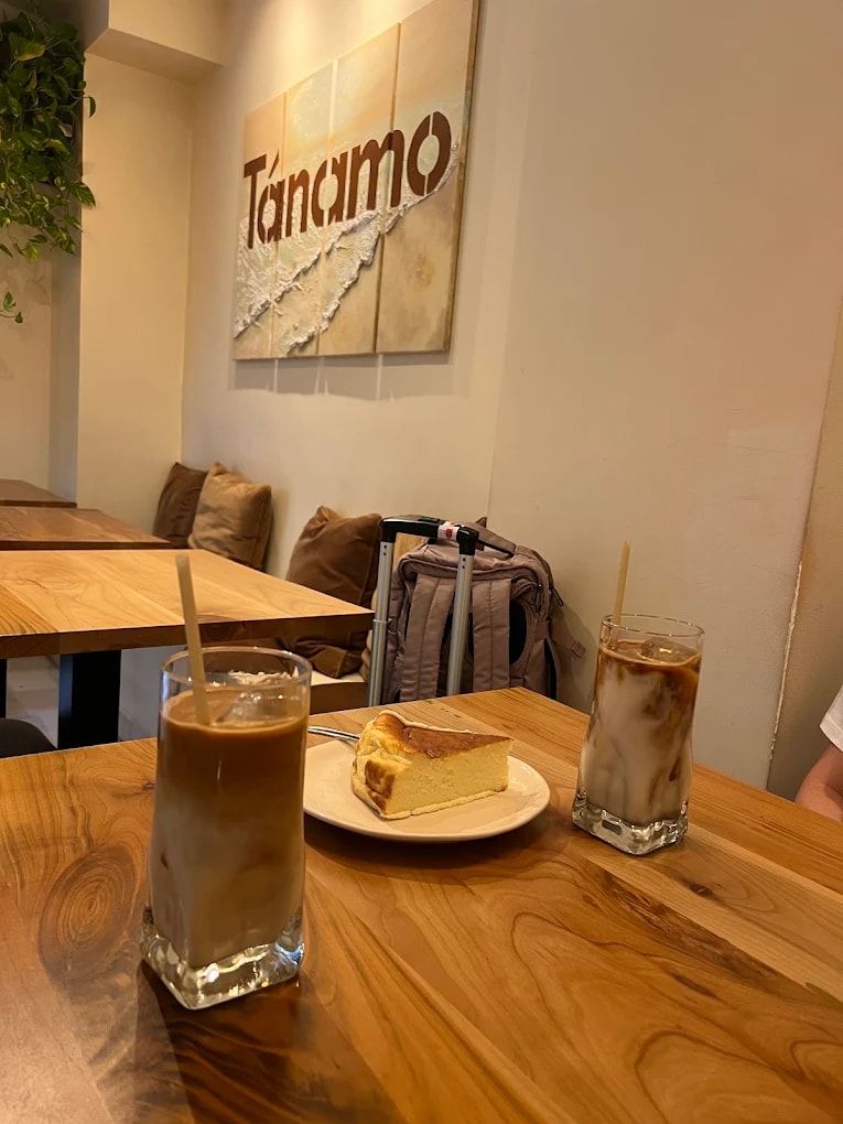 Cafés con hielo y cheesecake sobre la mesa de roble, con el logo de Tánamo en la pared